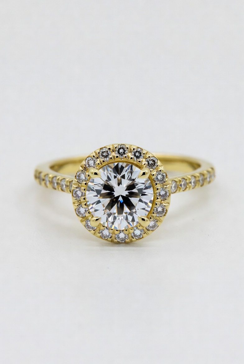 Round brilliant lab-grown diamond framed by a pavé halo of accent diamonds on a yellow gold band with diamonds along the shank