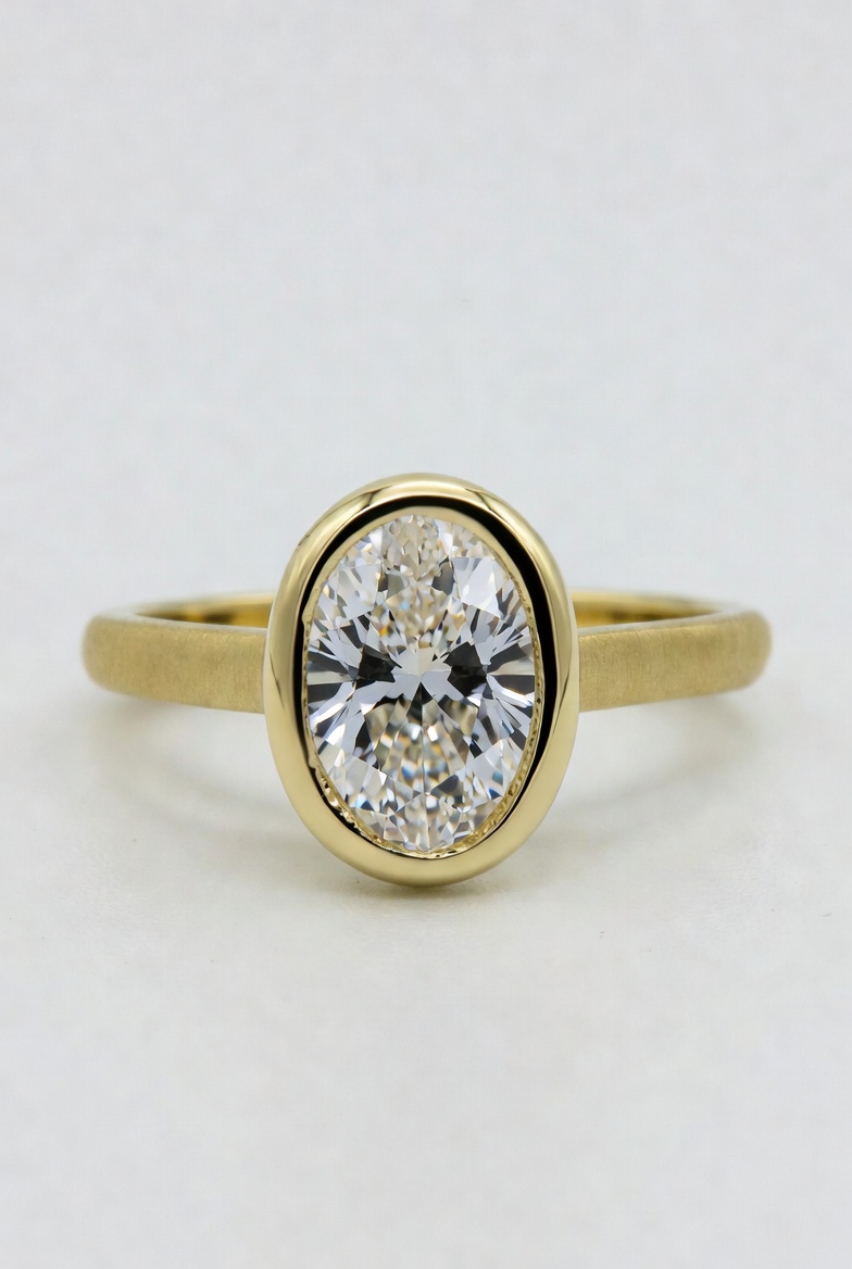Oval lab-grown diamond fully bezel-set in a smooth yellow gold rim on a satin-finished band